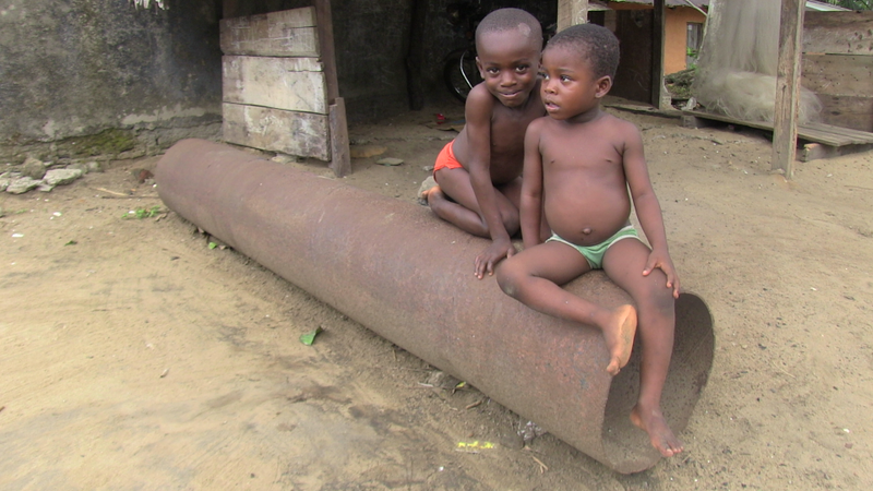 Two children sit on a rusted pipeline in the Niger Delta.